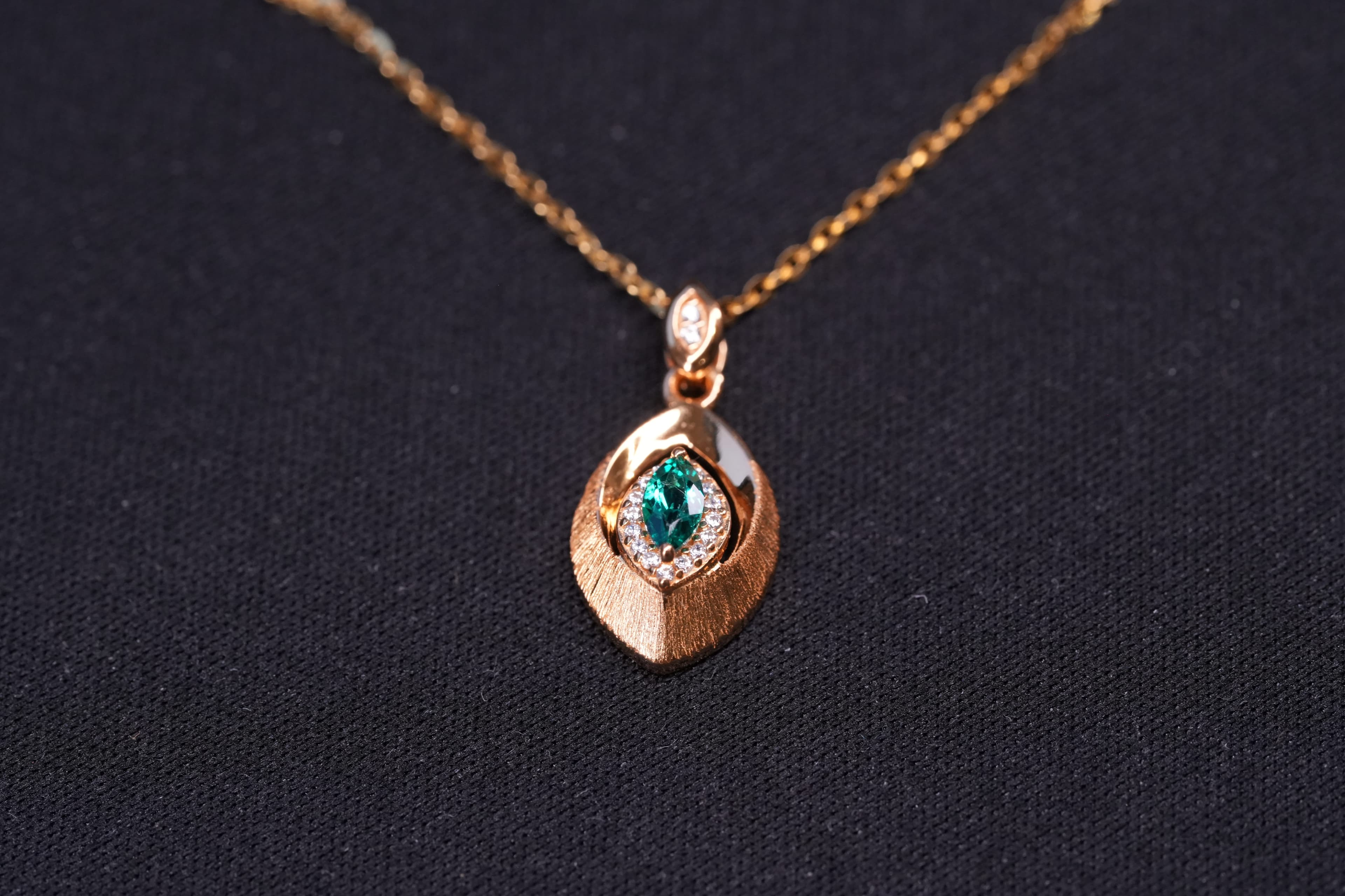 Gold-plated sterling silver pendant necklace featuring a marquise-cut green lab-created emerald, clear accent stones, and a sculptural leaf-inspired design.